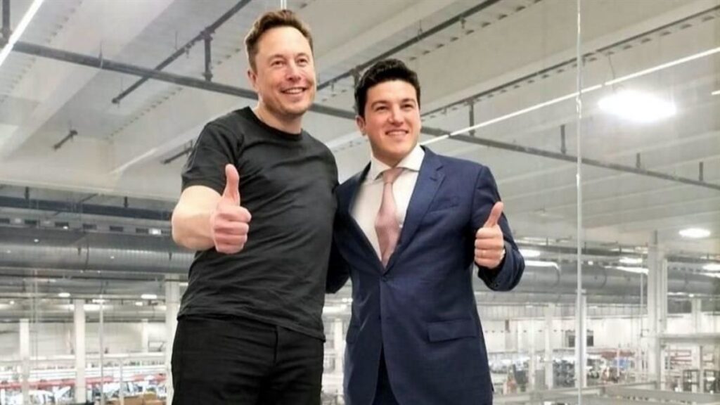Cifra-que-el-gobierno-de-nuevo-leon-ofrecio-a-elon-musk - La Sultana Informa Two Men in a Factory-like Space Smile and Give Thumbs Up; One Wears a Black T-shirt, the Other a Blue Suit and Pink Tie. - La Sultana Informa